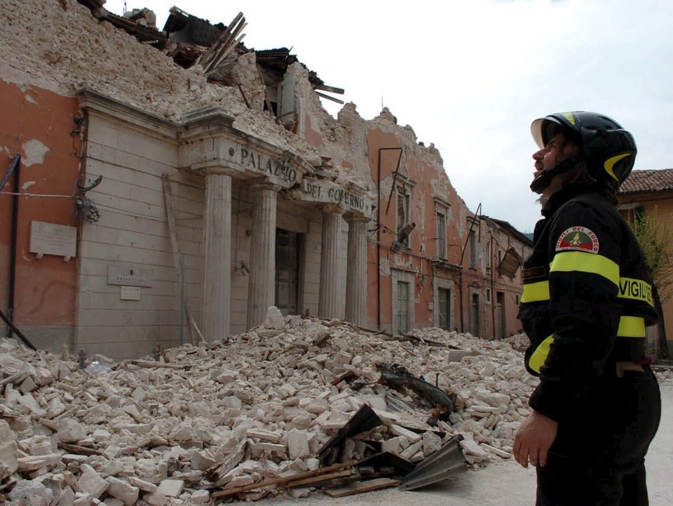 Ein Feuerwehrmann steht vor einem stark beschädigten Palazzo.