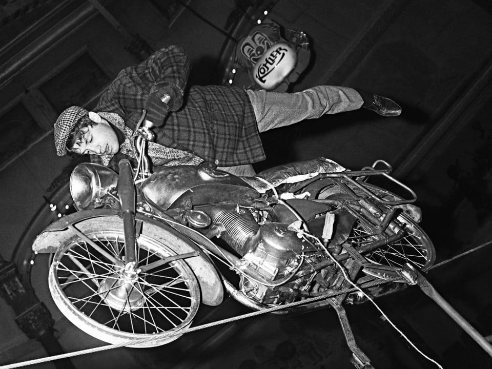 Belmondo 1963 mit einem Motorrad auf einem Hochseil balancierend.