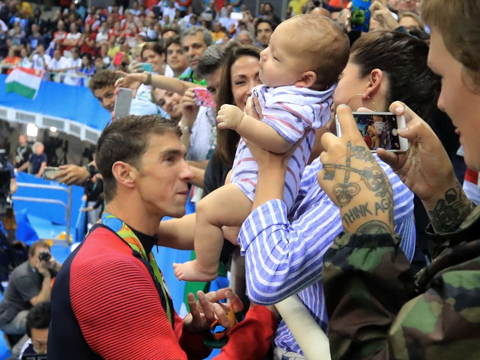 Michael Phelps' Verlobte hält ihm ein Baby entgegen.