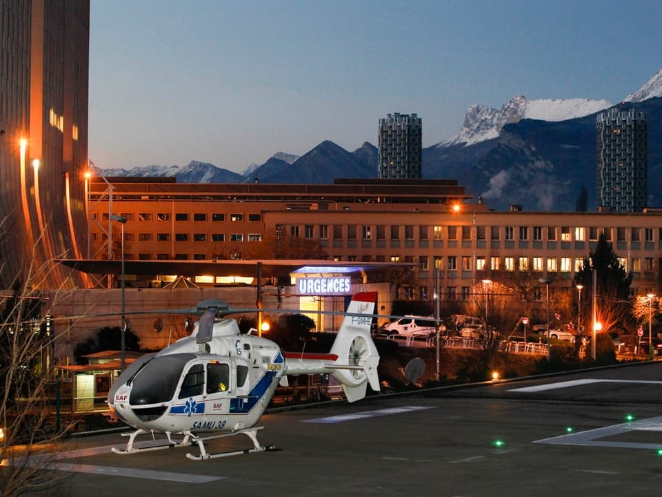 Ein Helikopter steht vor einem grossen Gebäude, im Hintergrund sind Berge zu sehen.