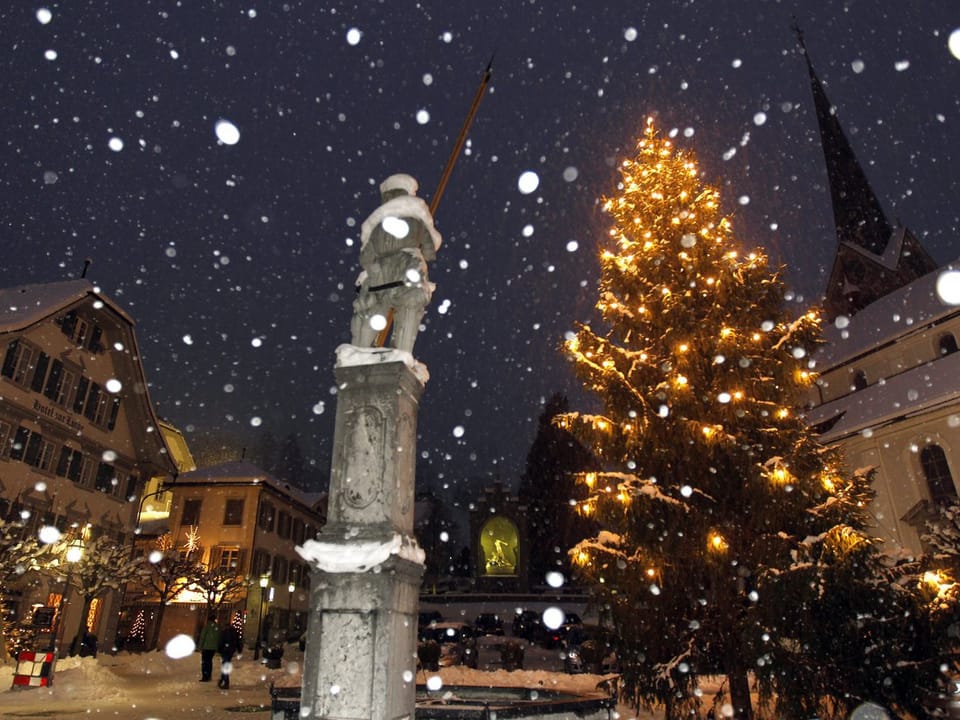Der Dorfplatz in Stans (Nidwalden): Schneeflocken fallen, im Hintergrund ein beleuchteter Weihnachtsbaum.