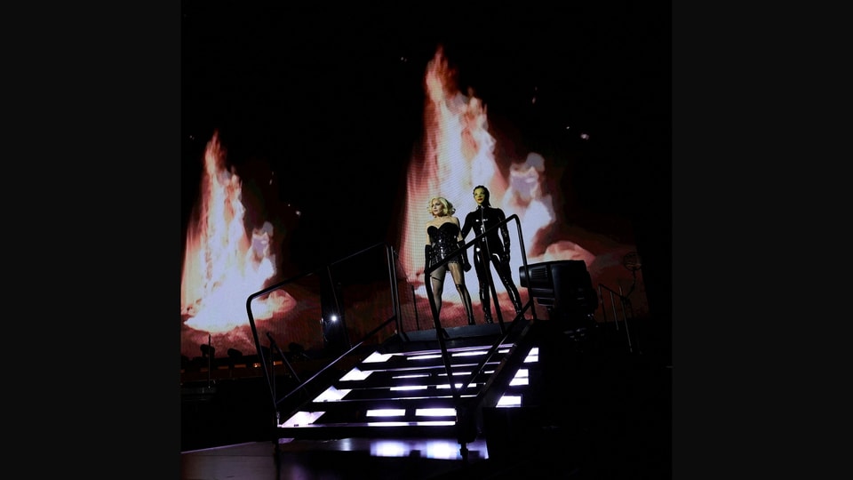 Madonna und eine Tänzerin auf einer Treppe, dahinter Flammen
