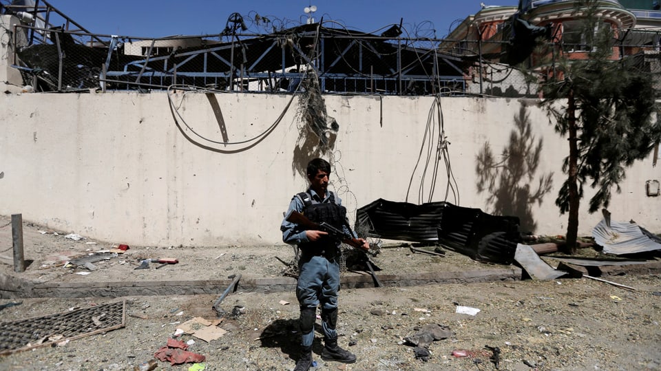 Afghanischer Soldat mit seinem Maschinengewehr vor dem zerbombten Haus. 