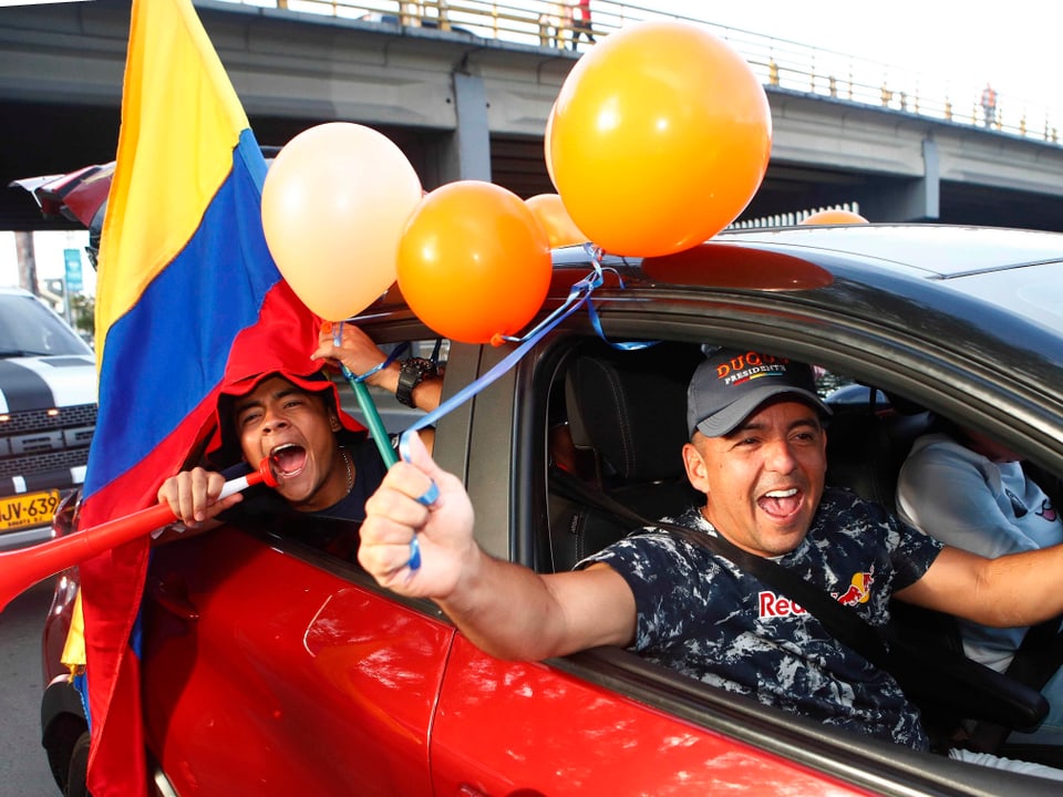 Männer in einem Auto halten die kolumbianische Flagge.
