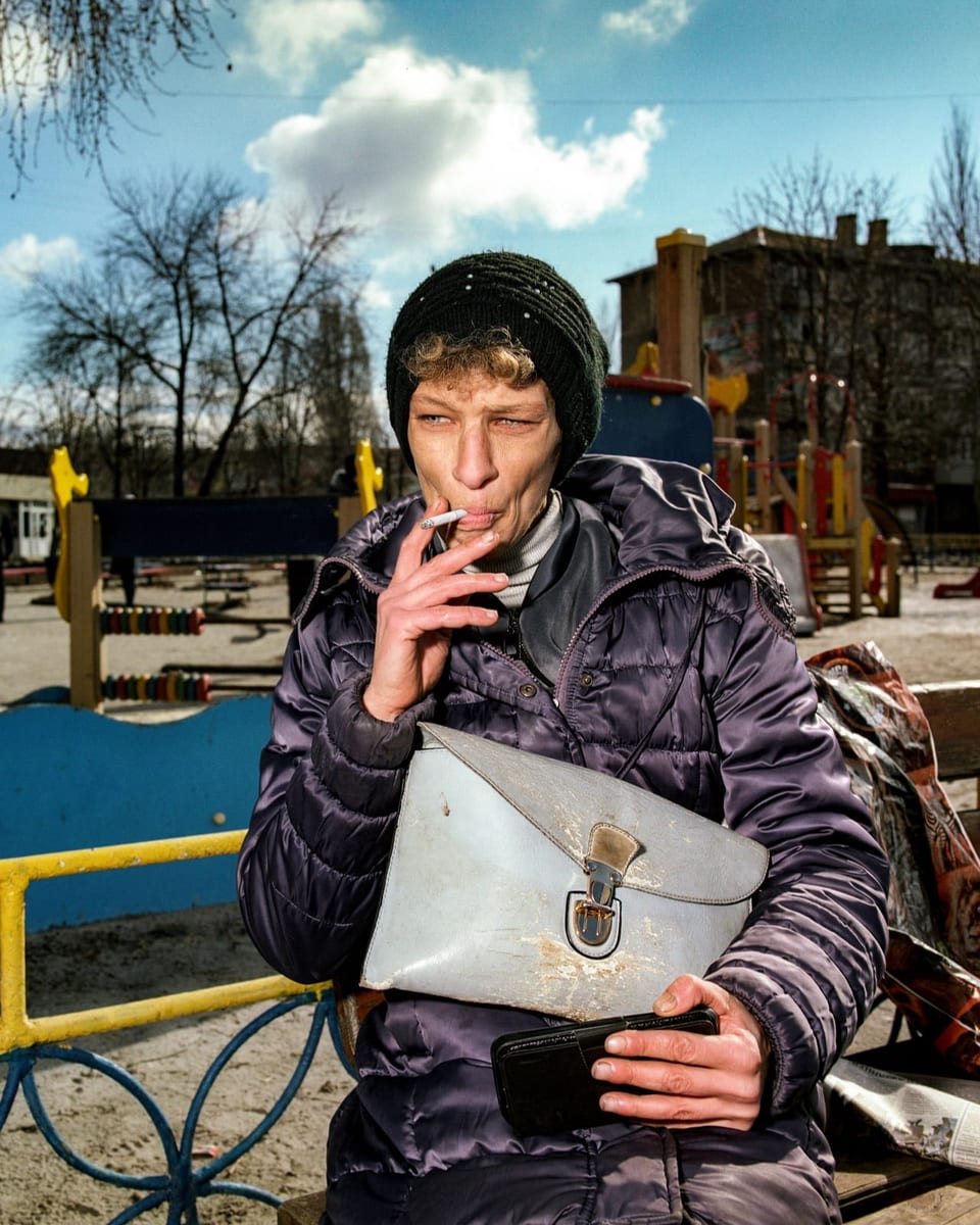 A woman with a lid sits on the bench, smokes a cigarette and looks into the distance.