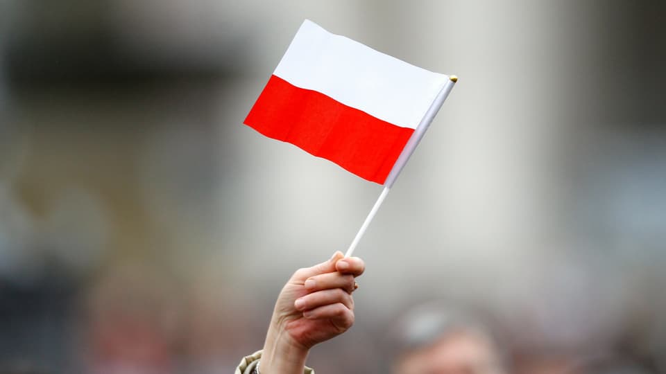 Eine Hand von einer Person. Sie streckt eine polnische Flagge in die Luft.