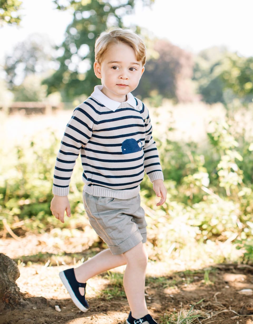 Prinz George geht im gestreiften Pullover und in beige-grauen Hosen durch den Garten.