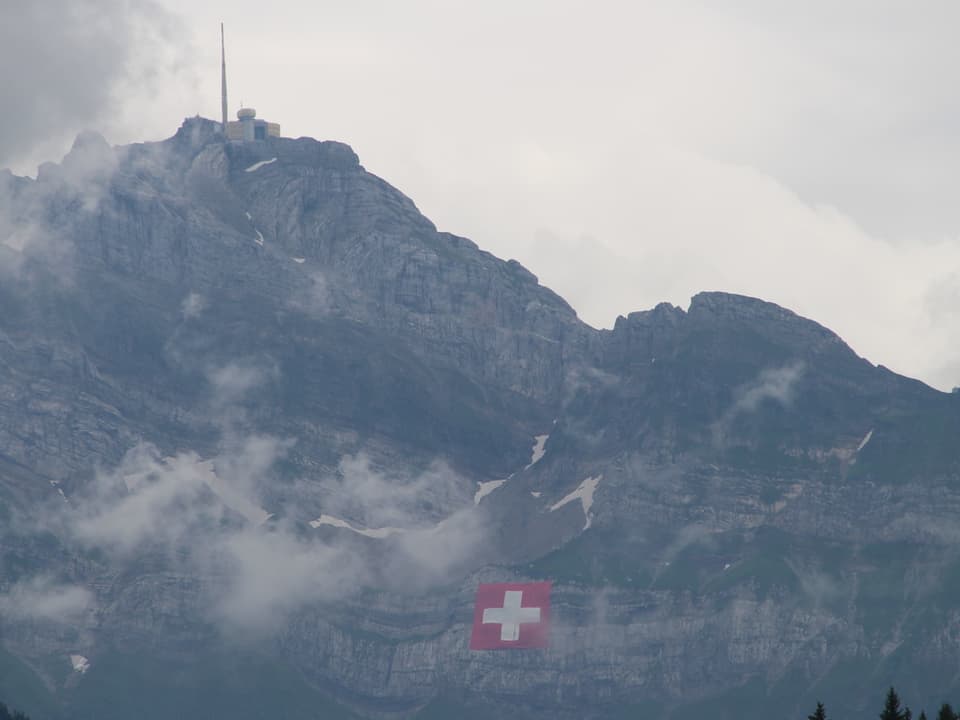 Säntis mit Wolken und Schweizer Flagge im Felsen
