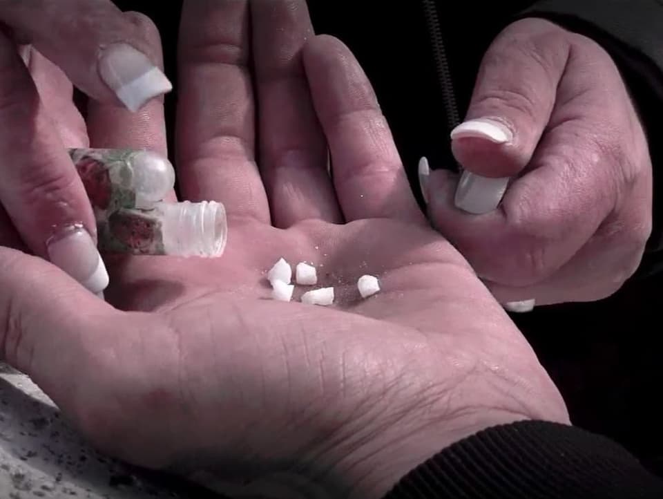 Eine Frau schüttet kleine Kokainsteinchen in eine offene Hand.