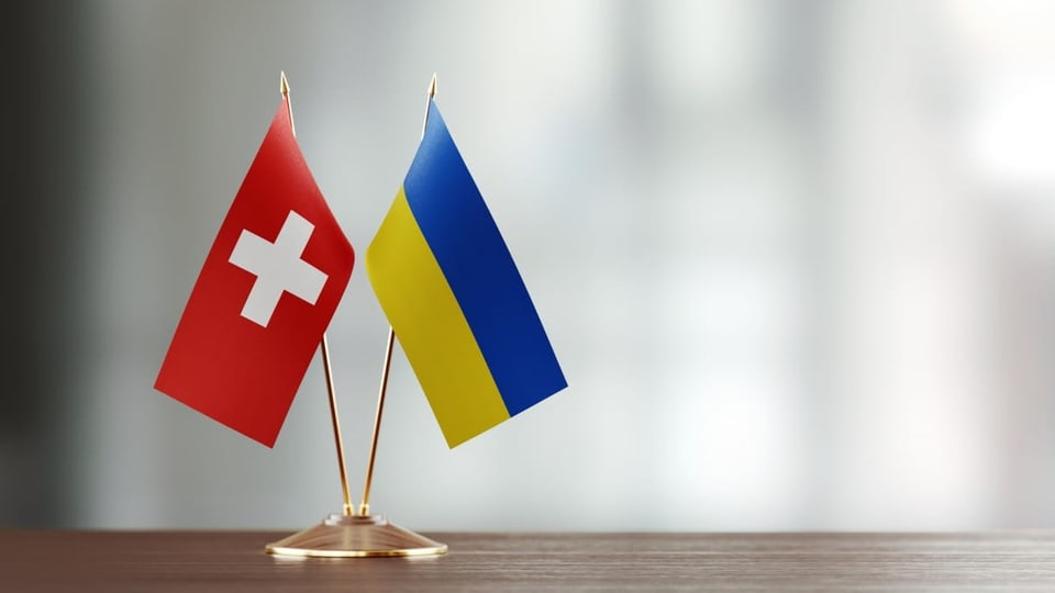 Schweizer und ukrainisches Flaggenpaar auf dem Schreibtisch vor unscharfem Hintergrund.