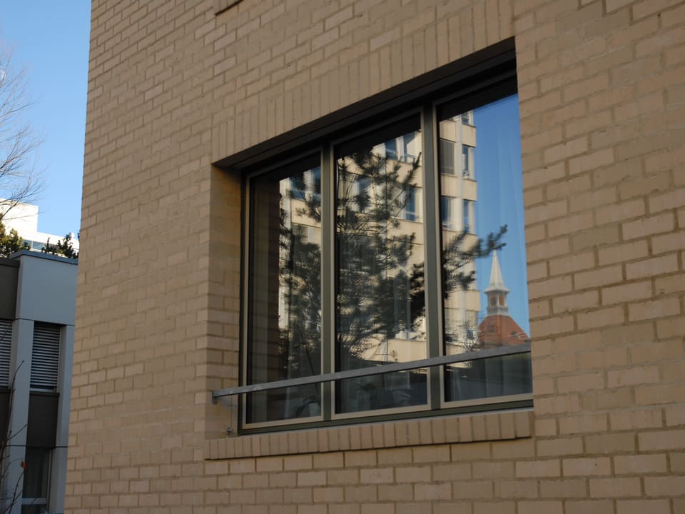 Fassade aus Klinkersteinen, im Fenster spiegeln sich die Häuser der Nachbarschaft.
