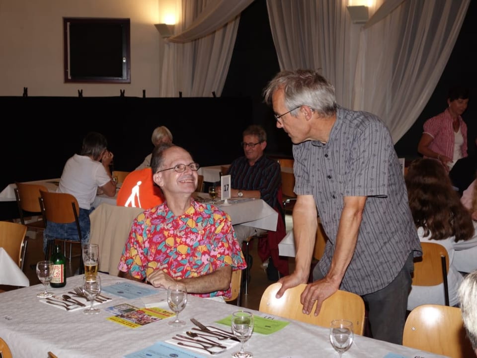 Ein Mann im Trachtenhemd redet in einem Festsaal mit einem Mann im Hawaii-Hemd