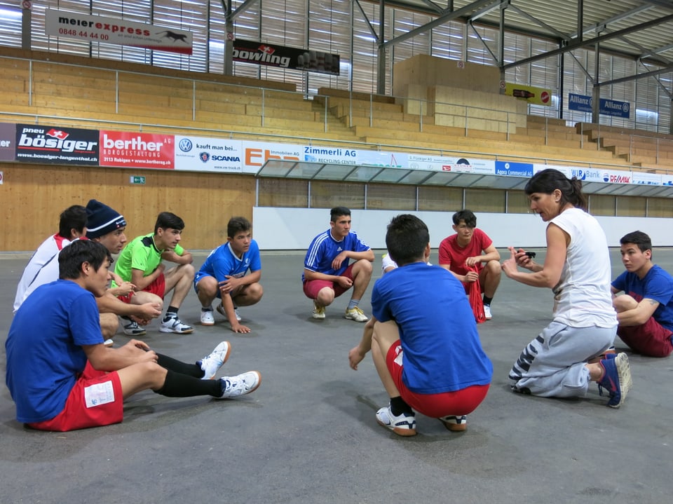 Sportlehrerin sitzt im Kreis mit jugendlichen Asylsuchenden.