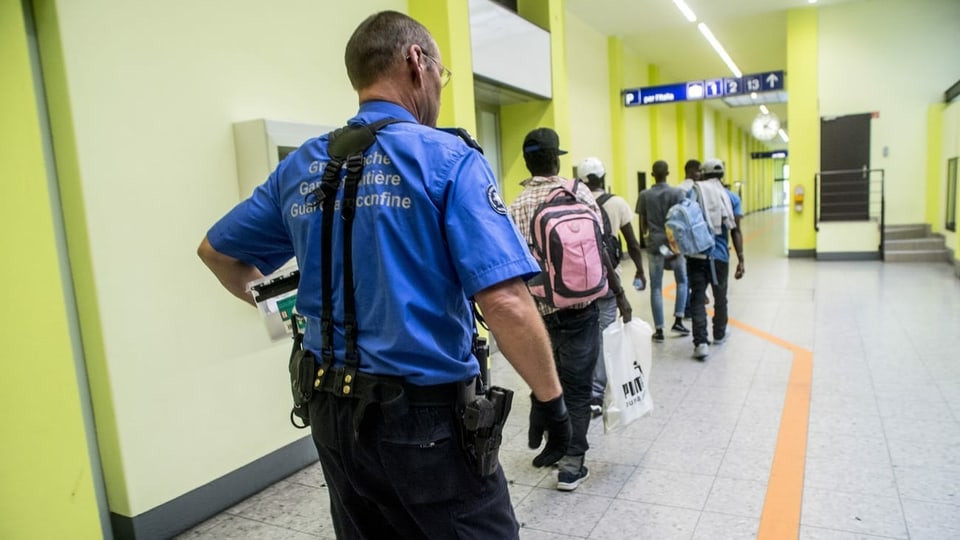 Ein Grenzwächter begleitet Migranten zur Personenkontrolle bei der Grenzkontrolle am Zoll des Bahnhofs Chiasso.