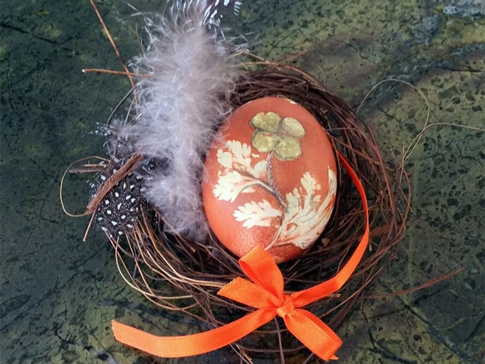 Ein selbst gefärbtes Osterei in einem Nest mit Federn.