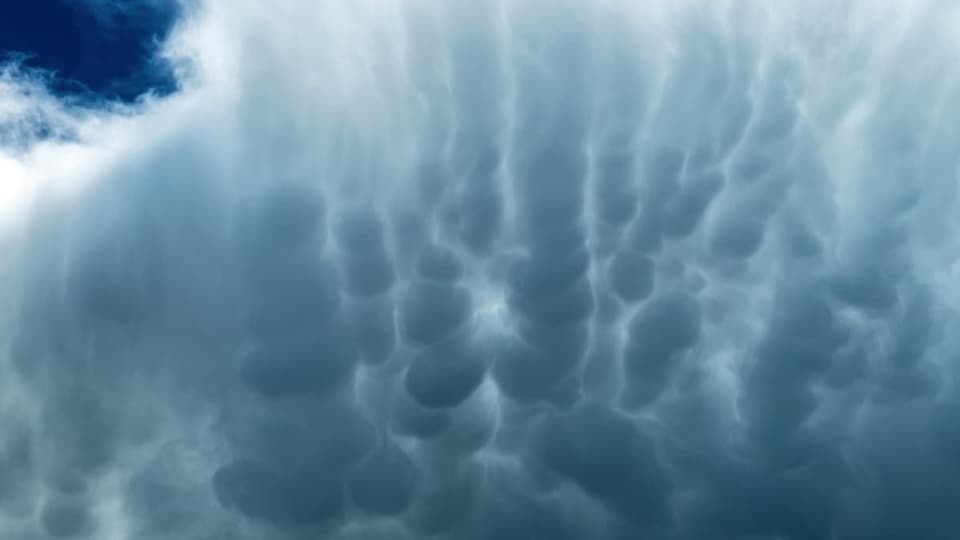 Blick an den bewölkten Himmel. Auf der dunklen Wolkenunterseite sind beutelartige Strukturen zu sehen. 