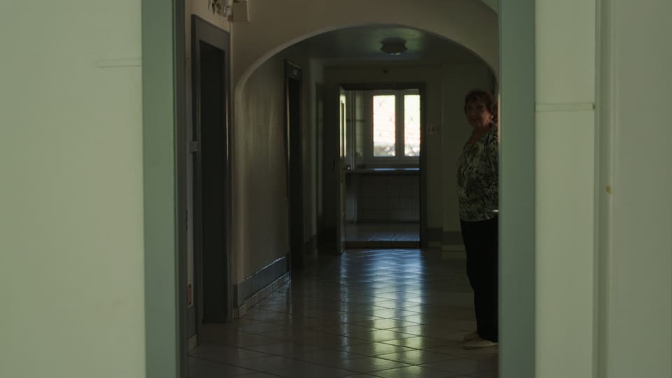 Person steht am Ende eines dunklen Flurs mit Türrahmen im Vordergrund.