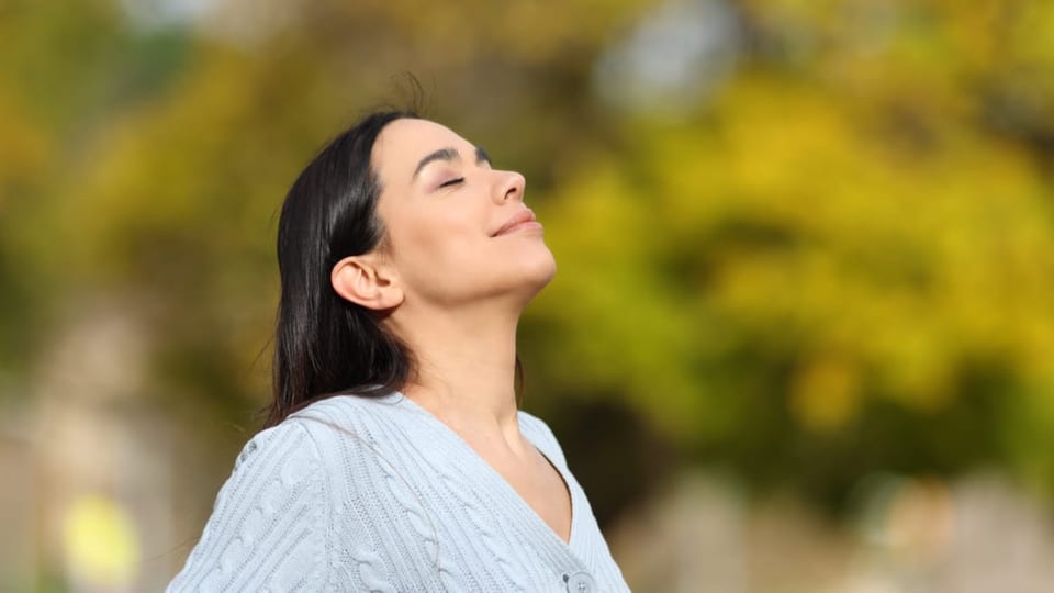 Eine Frau macht Atemübungen im Freien. Die Atemübungen können dabei helfen, den Körper und Geist zu entspannen. 