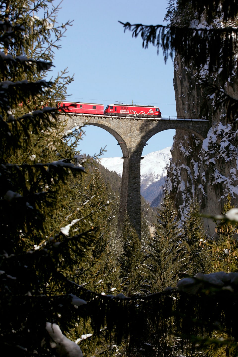 Ein roter Zug der Rhätischen Bahn überfährt das Landwasserviadukt auf der Albulalinie nahe Filisur.