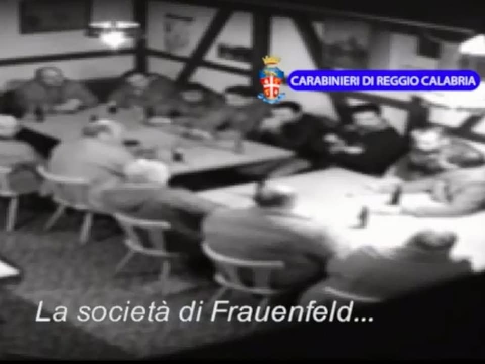 Ein Dutzend Männer sitzen an einem Tisch. Screenshot eines Überwachungsvideos.