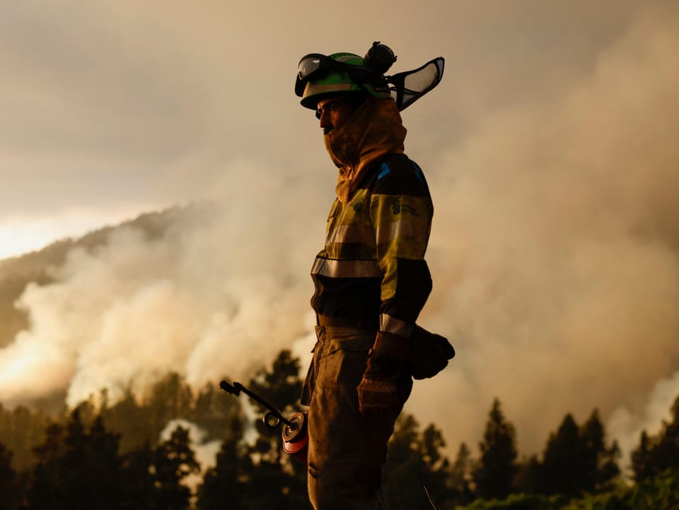 Ein Feuerwehrmann. Im Hintergrund steigt eine grosse Rauchsäule auf.