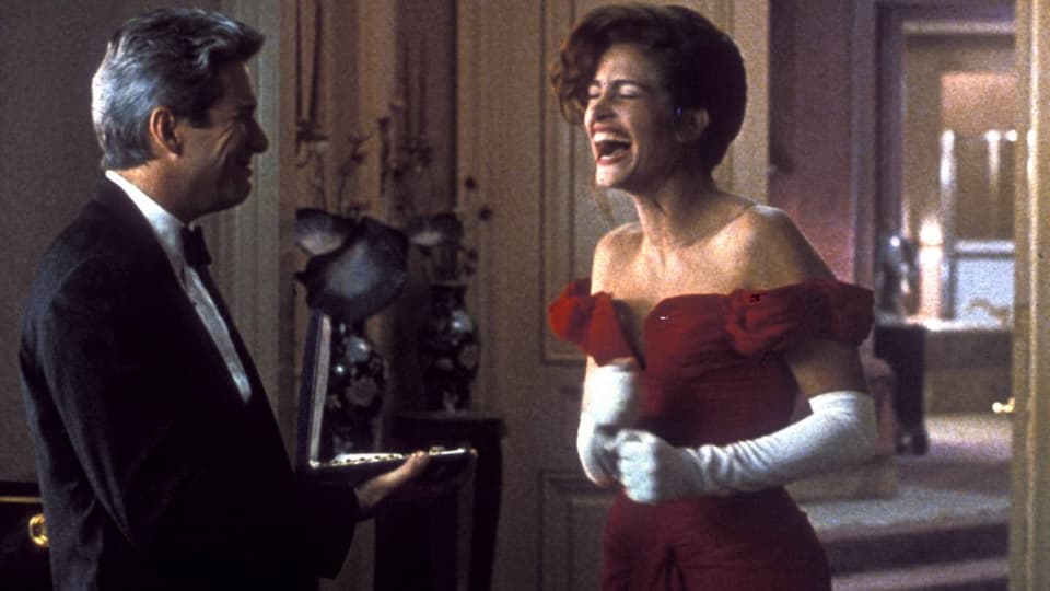 Links ein Mann mit grauem Haar, lächelt. Rechts Frau in rotem Kleid, lacht mit offenem Mund.