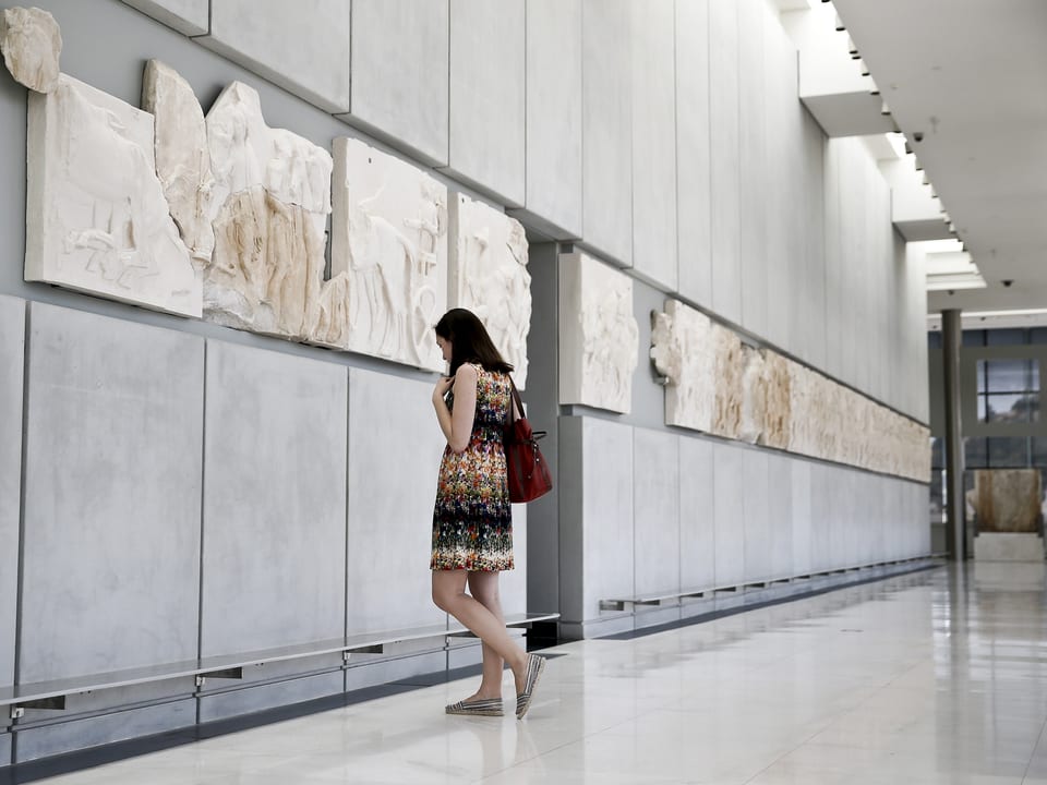 Eine Frau ist in einer Ausstellung und betrachtet etwas an der Wand. 