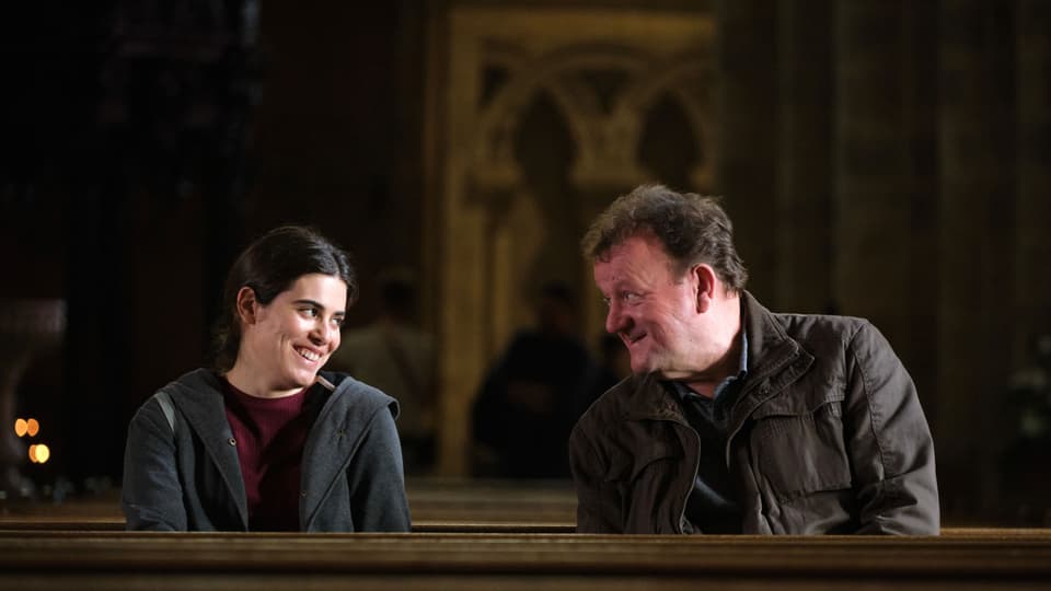 Eine Frau und ein Mann sitzen lächelnd auf einer Kirchenbank
