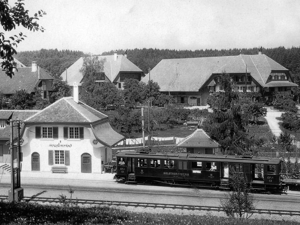 Schwarz-weiss-Bild mit Zügli neben altem Bahnhof, im Hintergrund Bauernhäuser