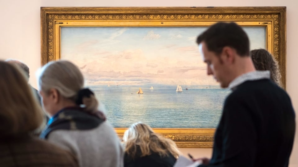 Szene aus der Ausstellung. Menschen stehen vor dem Gemälde «Das britische Reich» von John Bratt. Es zeigt Wasser, Schiffe und Wolken.