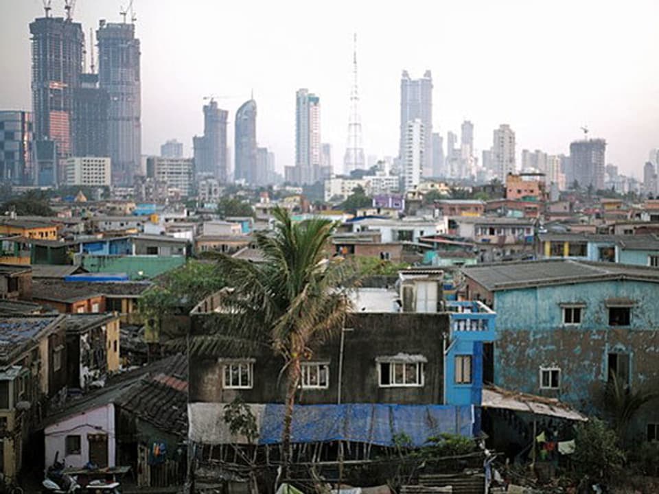 Slum im Vordergrund, Hochhäuser im Hintergrund. 