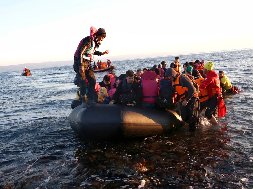 Ein Gummiboot voller Menschen im knietiefen Wasser, Helfer stehen bereit.