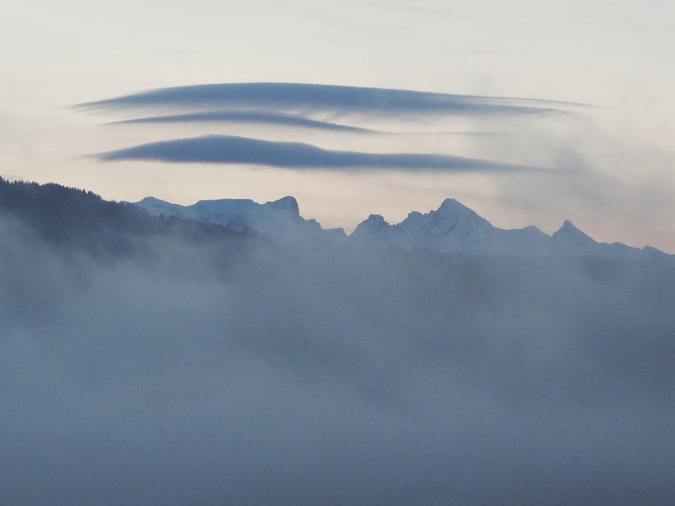 Unten Nebel, darüber klarer Himmel mit Blick in die Schneeberge. Am klaren Himmel hat es lediglich drei linsenförmige Wolken. 