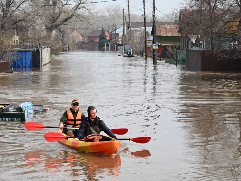 Zwei Männer rudern in einem Boot auf einer überfluteten Strasse.