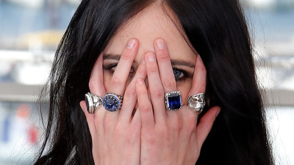 Eine Frau deckt sich mit den Händen ihr Gesicht ab. Sie trägt vier Ringe.