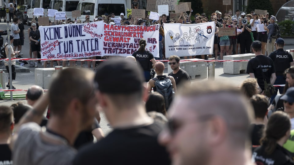 Zwei Frauen marschieren mit Transparent «Keine Bühne für Täter» und skandieren – im Hintergrund Menge.