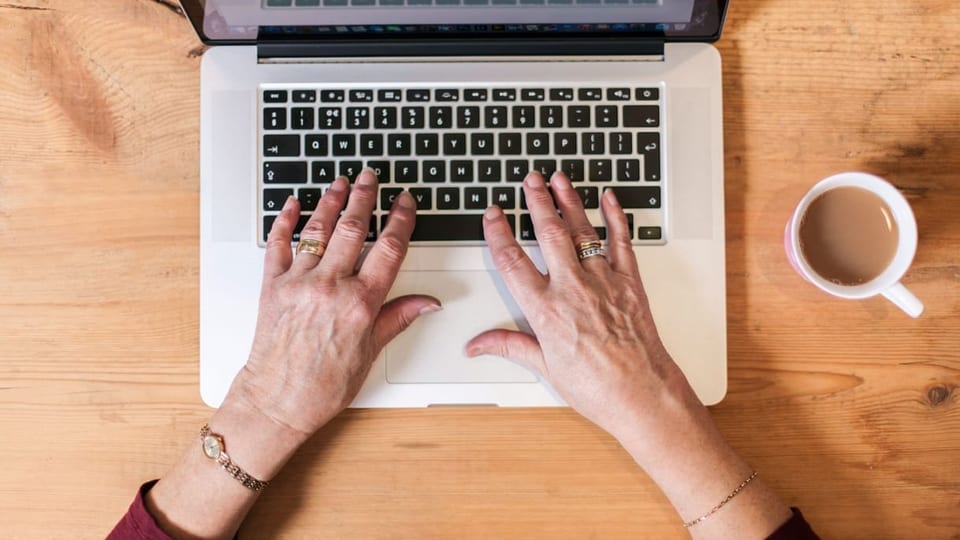 Ältere Frauenhände an einer Laptop-Tastatur.