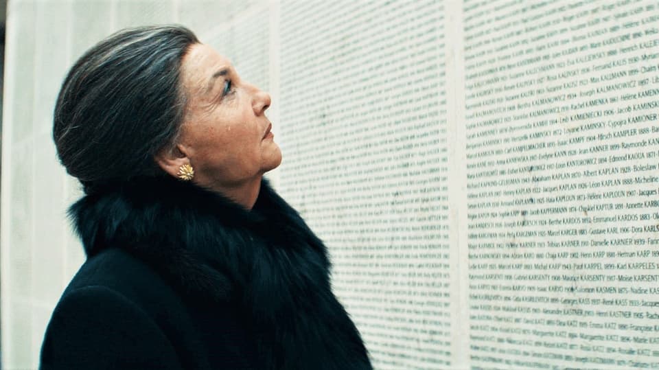 Eine Frau steht vor einer Mauer, auf der Millionen von Namen geschrieben sind.