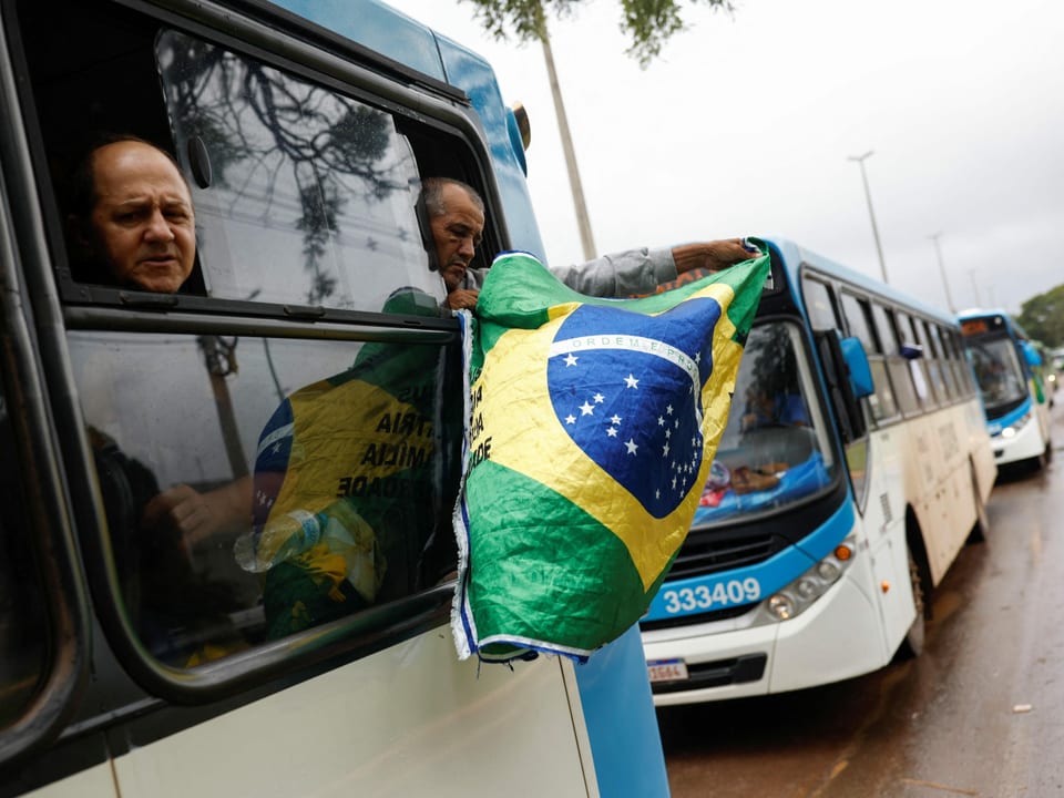 Männer halten ihre Köpfe aus fahrendem Bus, einer schwenkt brasilianische Flagge