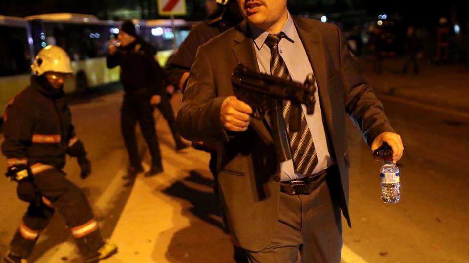 Ein Mann in Zivil mit einer Maschinenpistole.