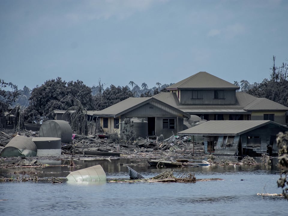 Ein zerstörtes Haus steht im Wasser, es treiben Trümmerteile umher.