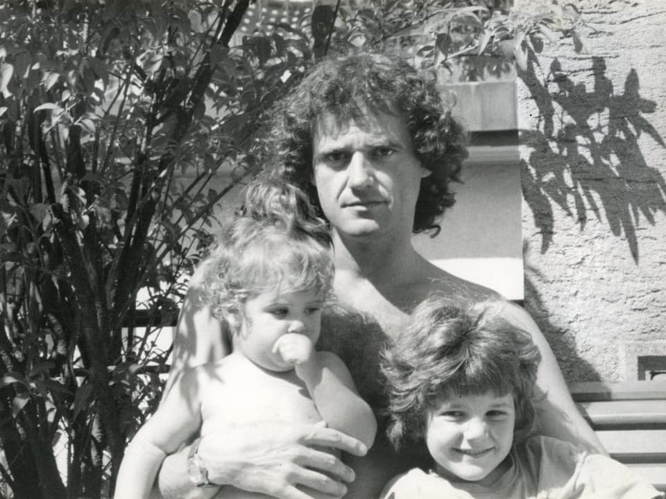 Ein Mann mit zwei kleinen Kindern auf dem Arm.