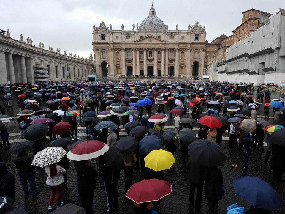 Tausende auf dem Petersplatz mit Regenschirmen.