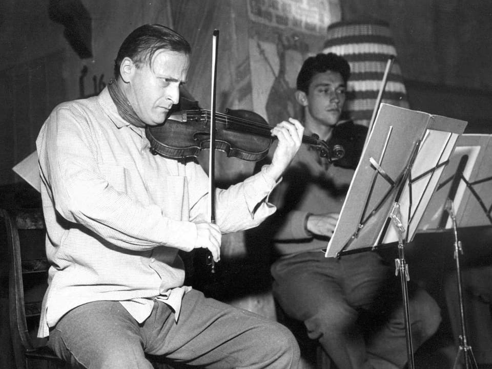 Zwei Männer spielen Geige und sitzen vor ihren Notenständern.