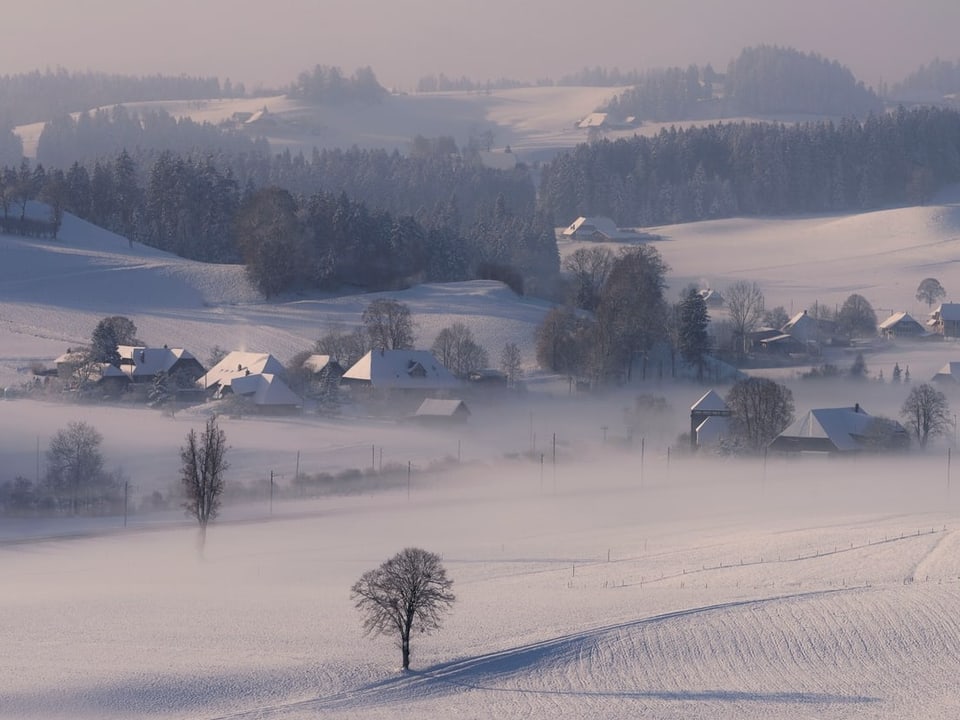 Blick auf eine verschneite Voralpenlandschaft mit einem kleinen Dorf