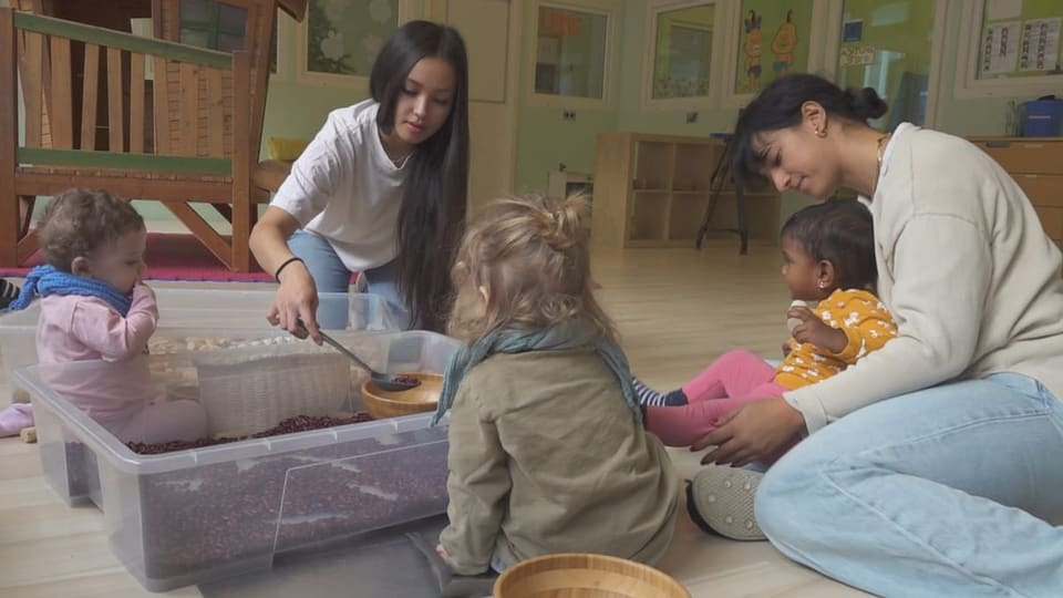 Betreuerinnen mit Kleinkindern in einer Kita, am Boden sitzend