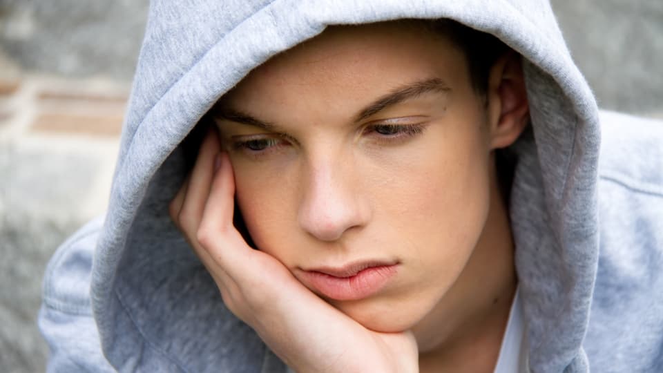 Jugendlicher stützt Kopf auf Hand, wirkt deprimiert.