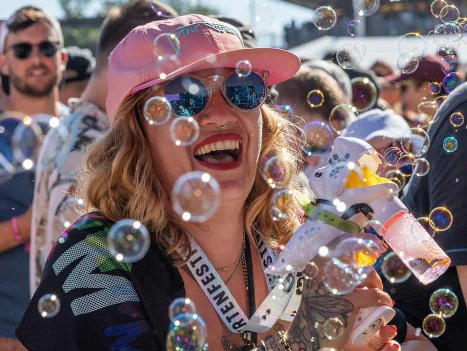 Eine Frau mit pinkem Käppli produziert Seifenblasen am Gurtenfestival