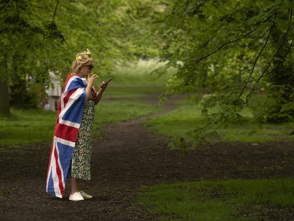 Frau mit umgehängter Flagge und Krone auf dem Kopf raucht und schaut ins Handy