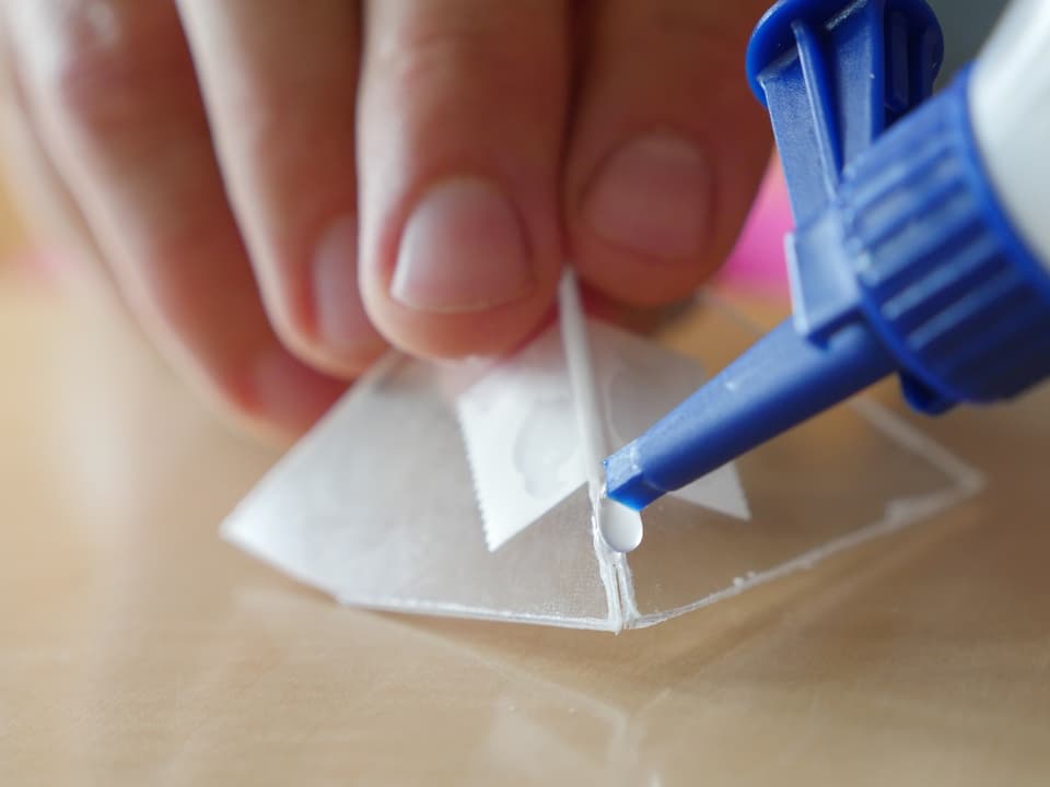 Kleine Trapeze aus Plastik werden mit Klebestreifen aneinandergeheftet.